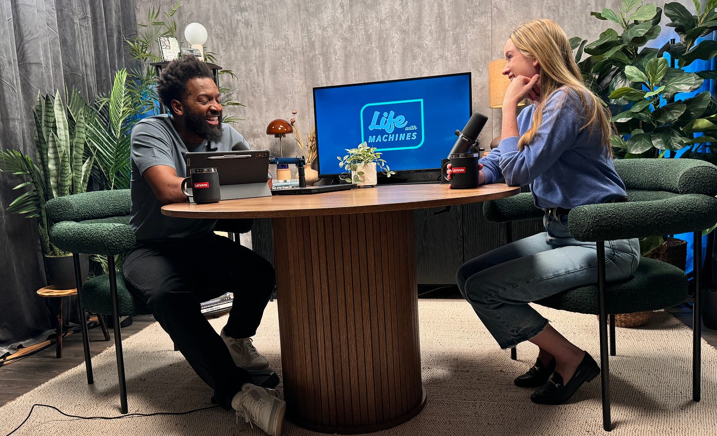 Photo from the studio used to record Life With Machines. Baratunde on left and Verity on right seated at circular table in center. They look happy