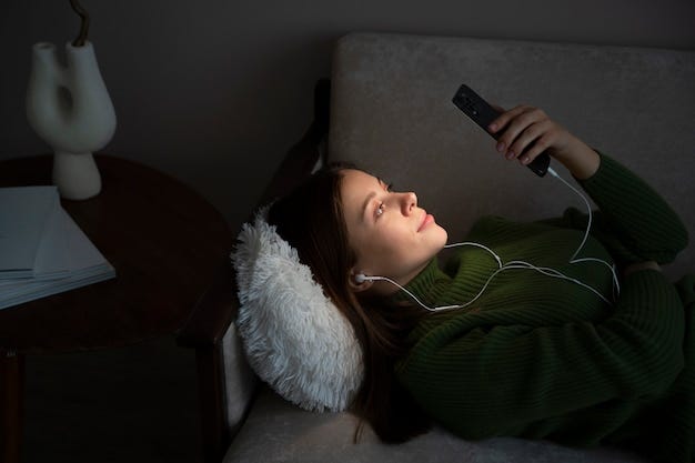 Woman listening music and looking at her smartphone while laying on the bed