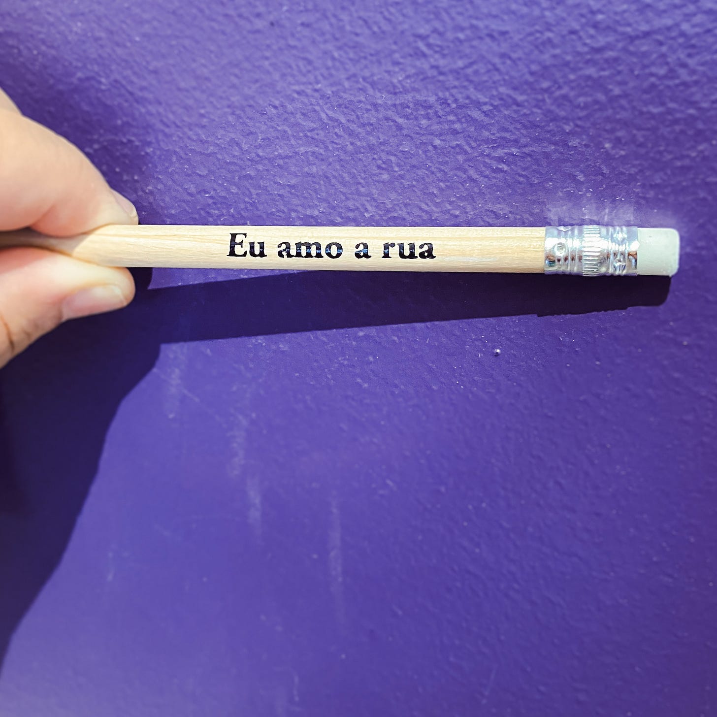 Um lápis no fundo lilás, com a inscrição "eu amo a rua"