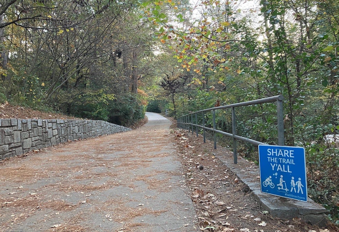 A sign by the trail says "Share the trail y'all" with silhouettes of walkers, a scooter and cyclist