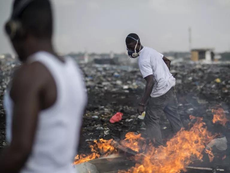 Young men on a large dumpsite shifting waste with an instrument as a fire burns the trash. Young men on a large dumpsite shifting waste with an instrument as a fire burns the trash.