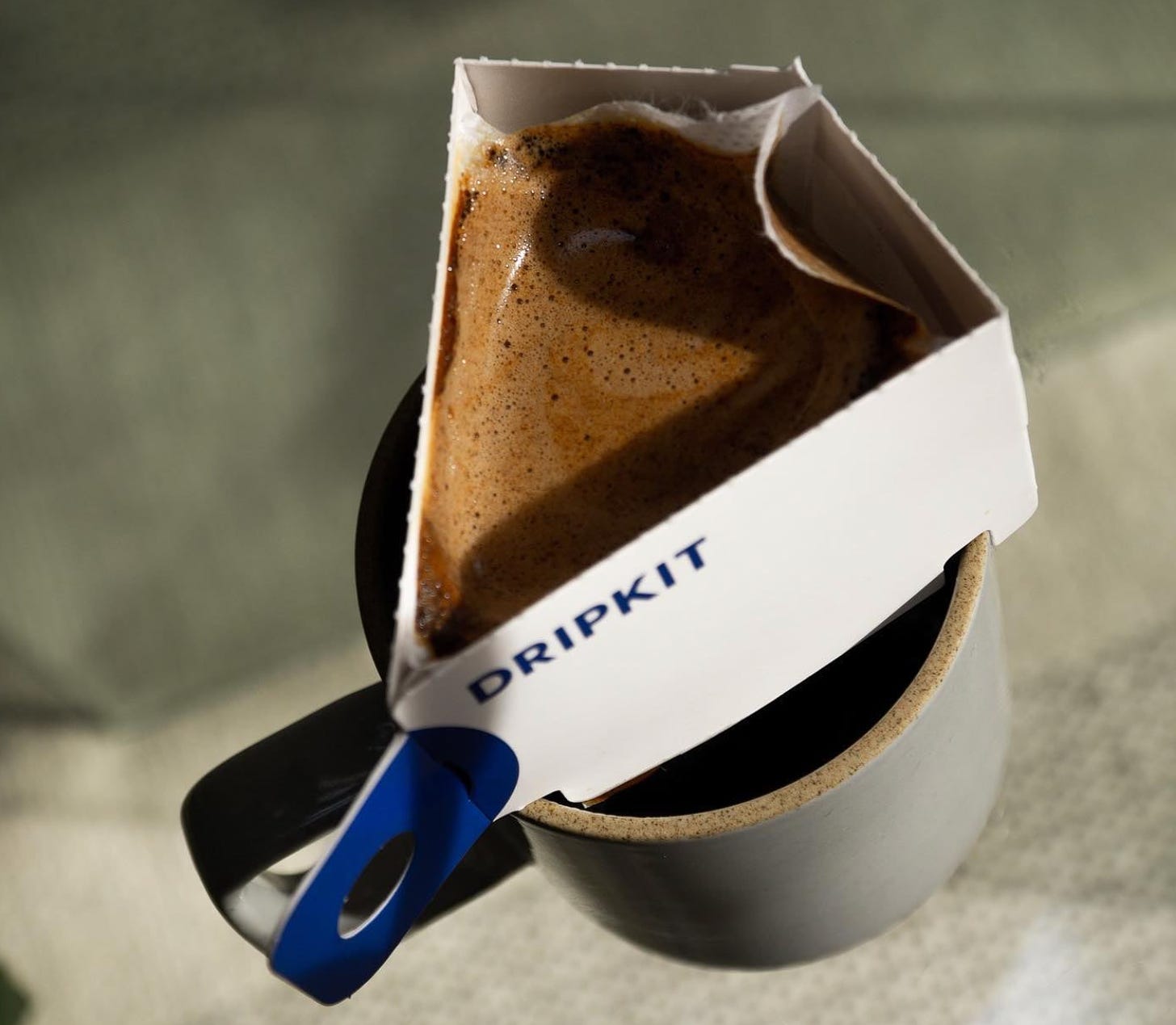 An overhead view of coffee brewing in a cardboard single-serving coffee brewer resting on a ceramic coffee mug.