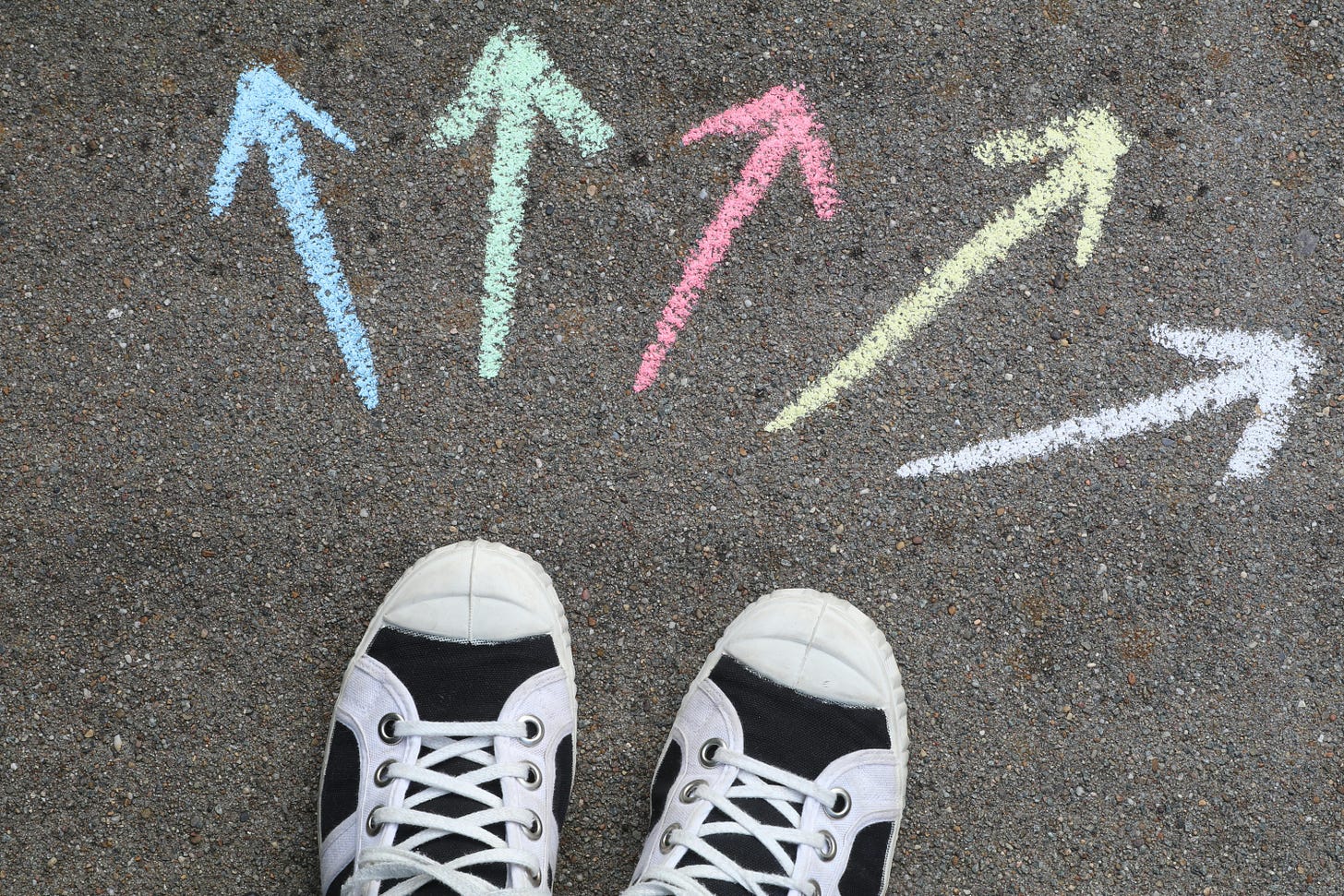 Looking down on a pair of shoes with arrows drawn in all directions on the pavement. Looking down on a pair of shoes with arrows drawn in all directions on the pavement.