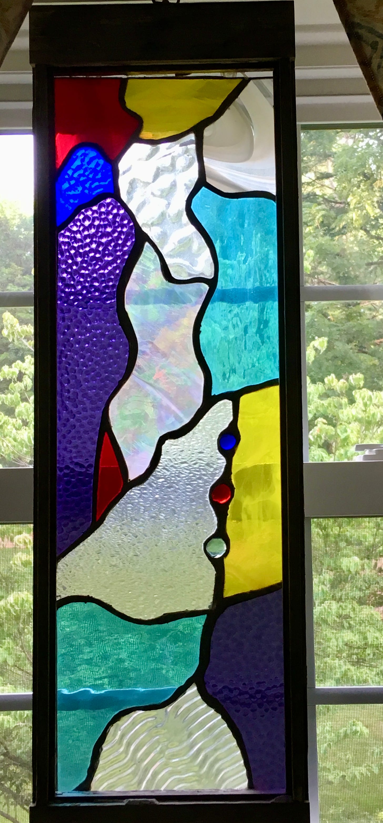 Abstract stained glass in board purples red yellow and turquoise in a wooden frame. Some of the stained glass is textured, including clear glass and some with iridescence.