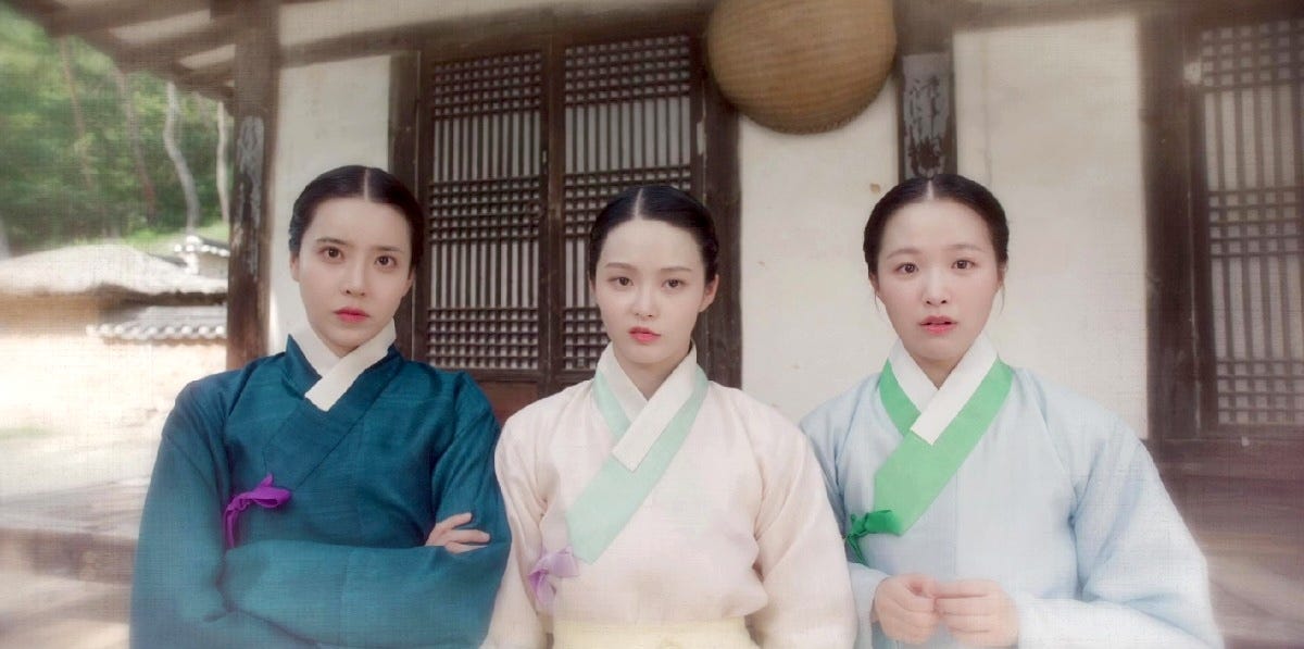 Three sisters in hanbok look into the camera with varying expressions