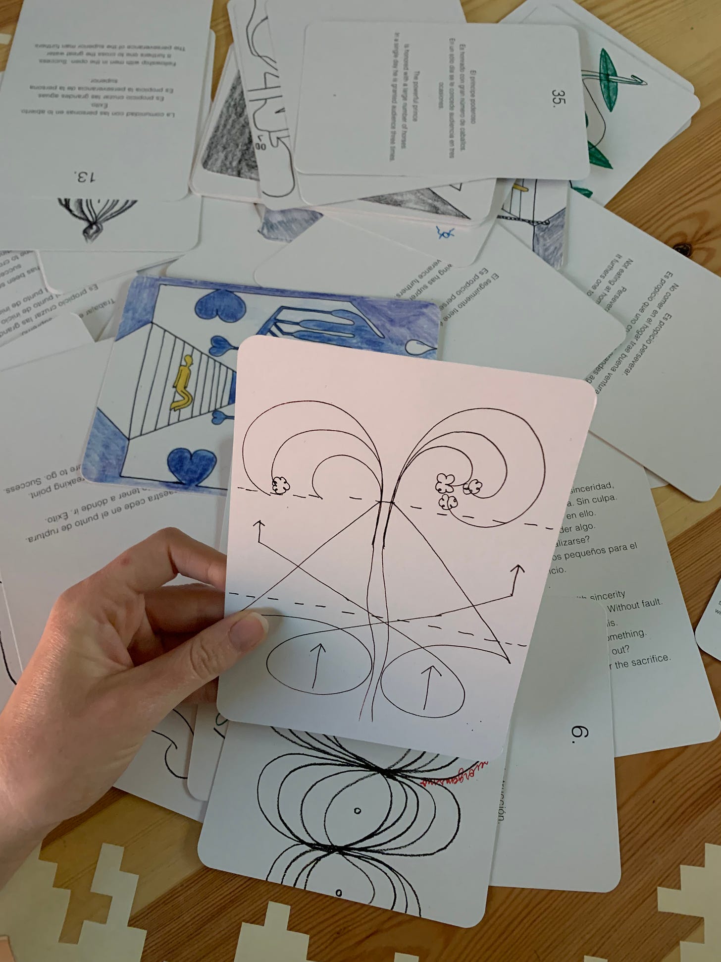 The wooden table with the cards scattered over it, a hand holding a card with an image on it.