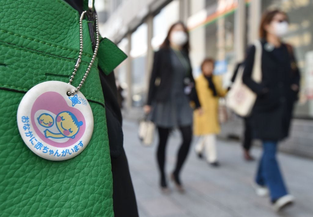 Pedestrians walk past a woman wearing a maternity badge on a street in Tokyo on March 3, 2016. (Toru Yamanaka—AFP/Getty Images)
