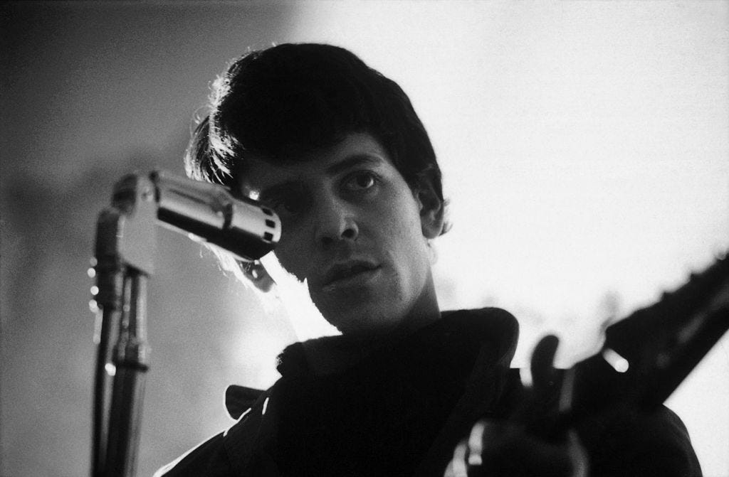 A black and white photo of Lou Reed performing in 1966, looking past the camera.