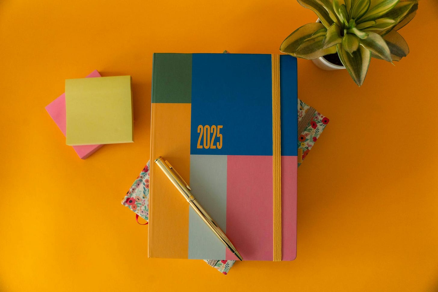 Photo of a colorful planner stack on a notebook with a pen on top next to Post-Its