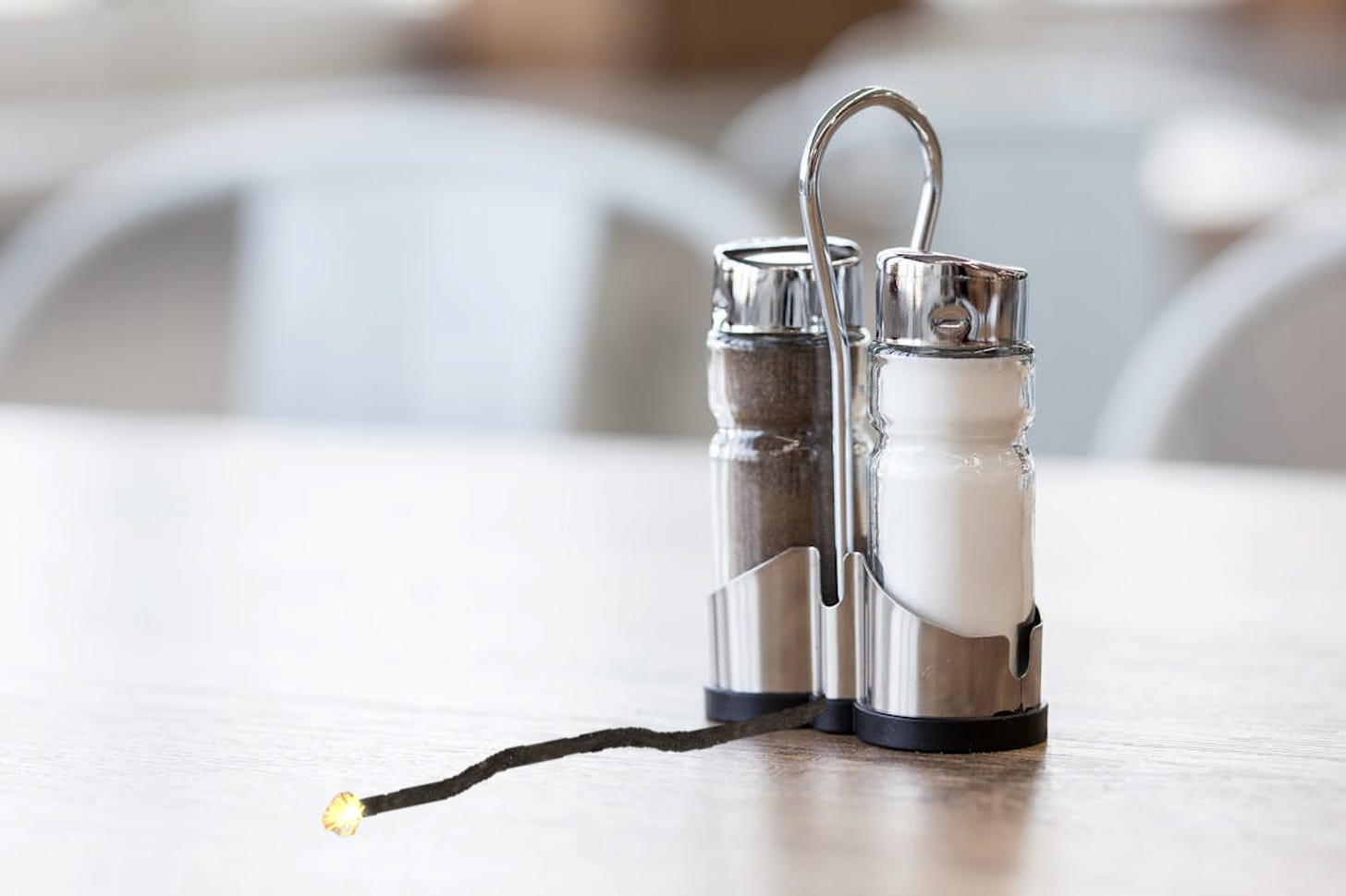 Picture of salt and pepper shakers on a  table -  with a lighted fuse attached to them.