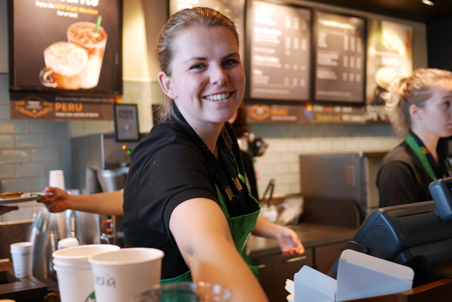 A Starbucks barista smiles as she hands over a coffee.