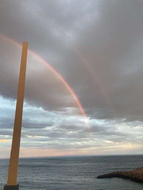 Image of a double rainbow before a dark cloud over an expansive body of water