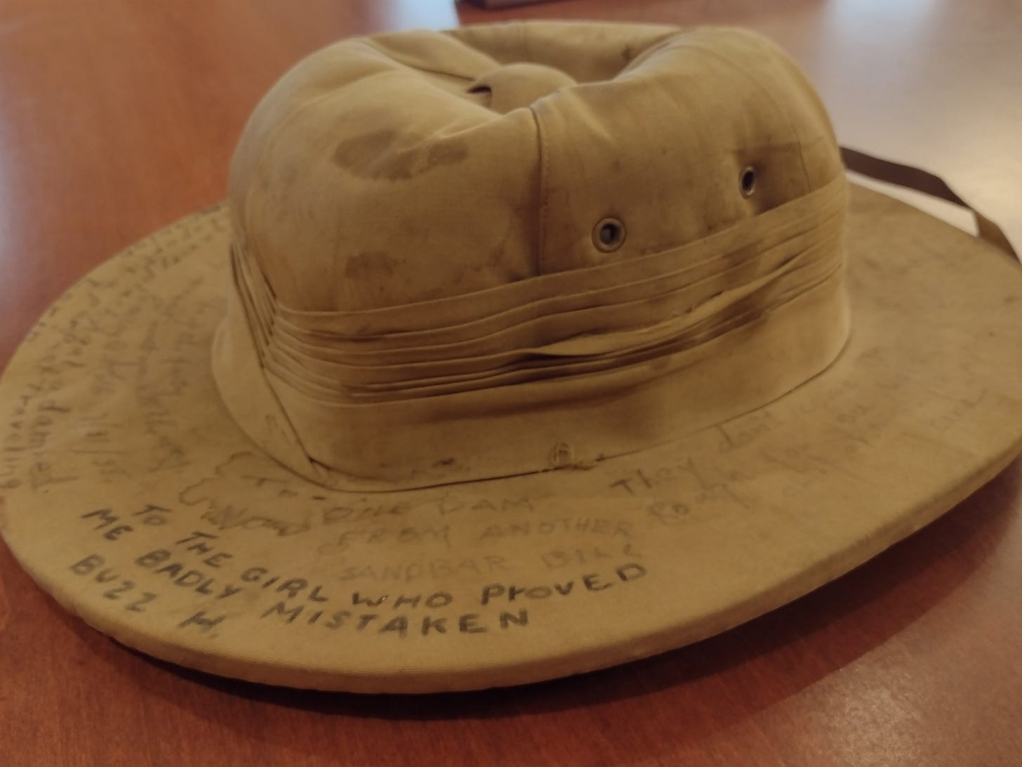 A slightly squash, tan pith helmet with signatures around the brim, including "to the girl who proved me badly mistaken -Buzz H."