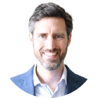 Professional headshot of a smiling man with salt-and-pepper beard wearing a blue blazer and checkered dress shirt against a white background.