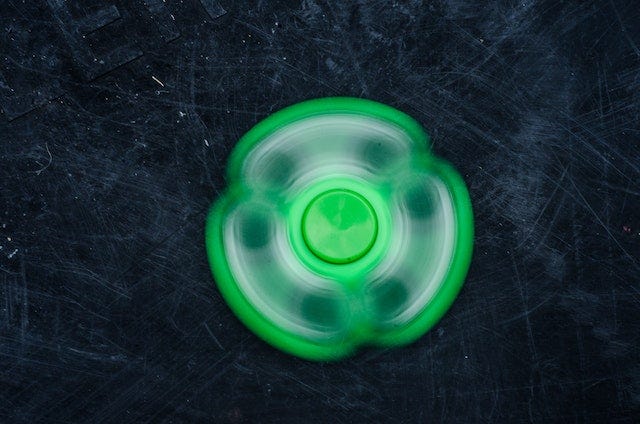 A green fidget spinner going spinny on a black background.