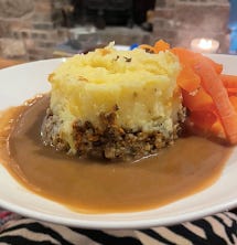 A haggis and mashed potato tower in a bowl, with carrots  and a cream and whiskey sauce surrounding it.