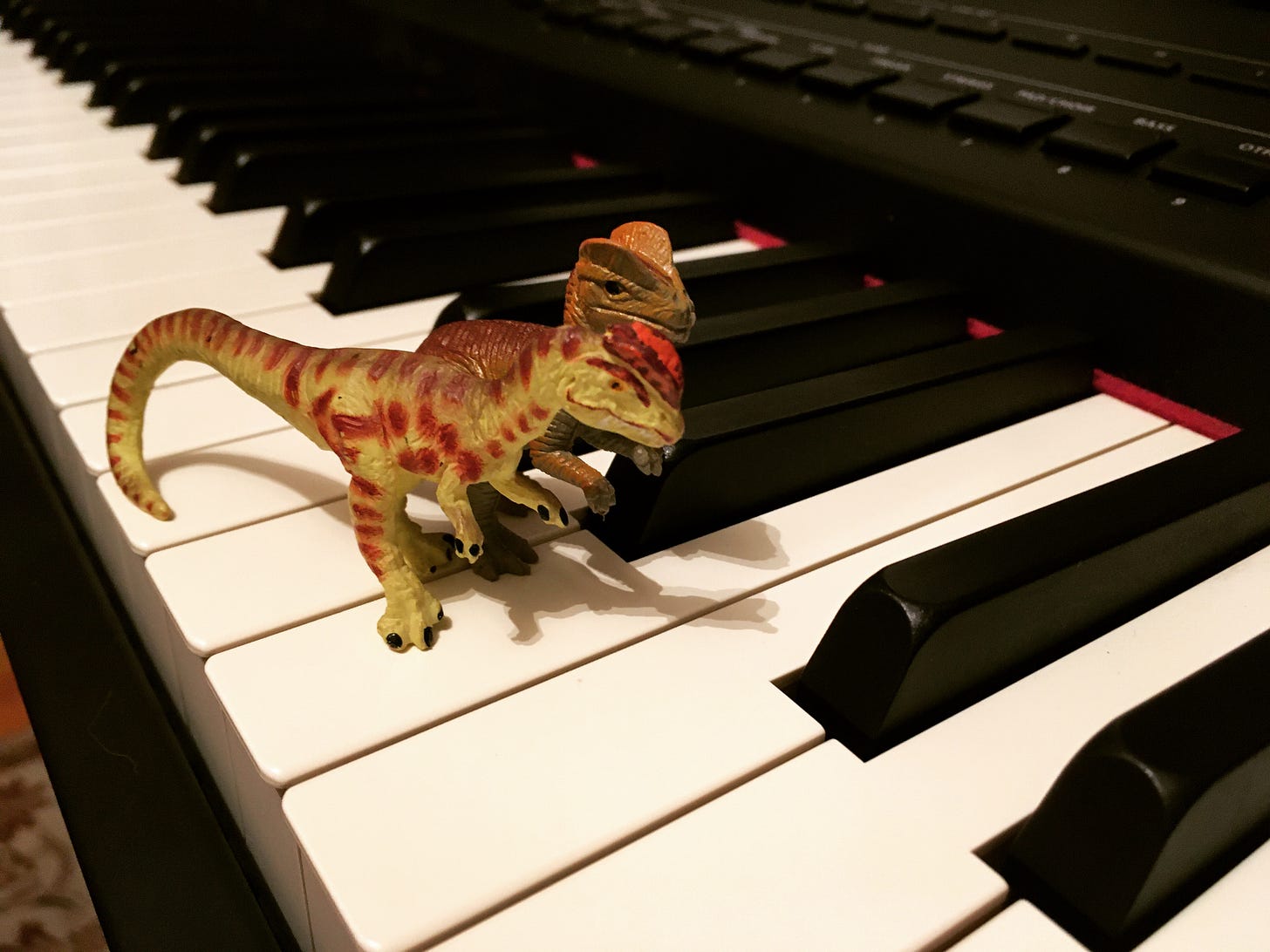 Two plastic specimens of Dilophosaurus sitting atop a piano keyboard, looking for food, perhaps a Sarahsaurus.