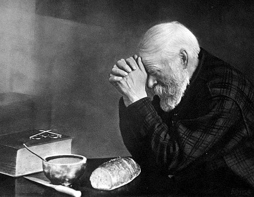 Black and white photo of an elderly traveling salesman saying grace over his bread.