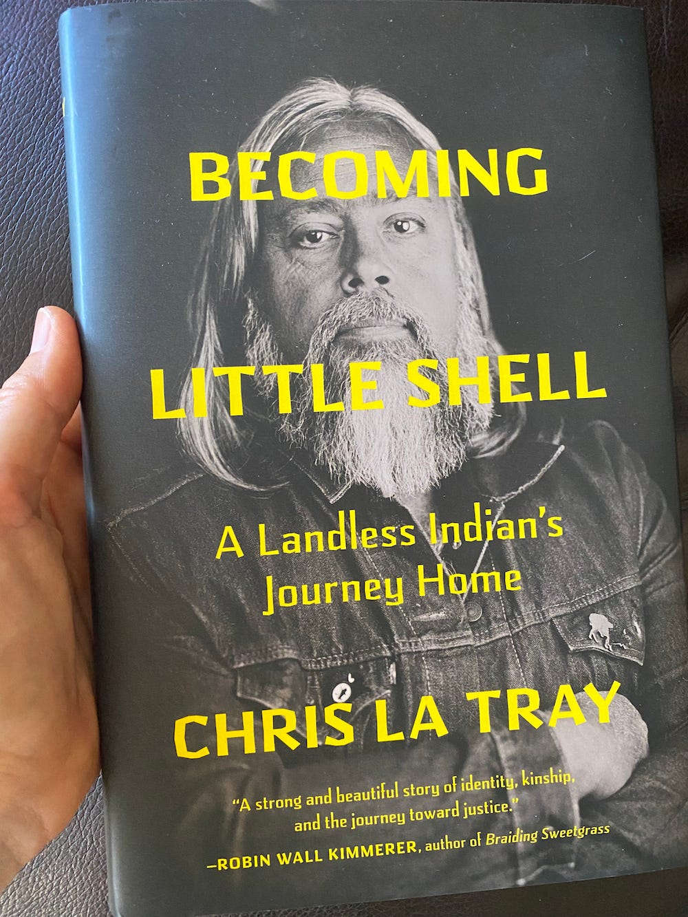 A hand holds Chris La Tray's book, Becoming Little Shell