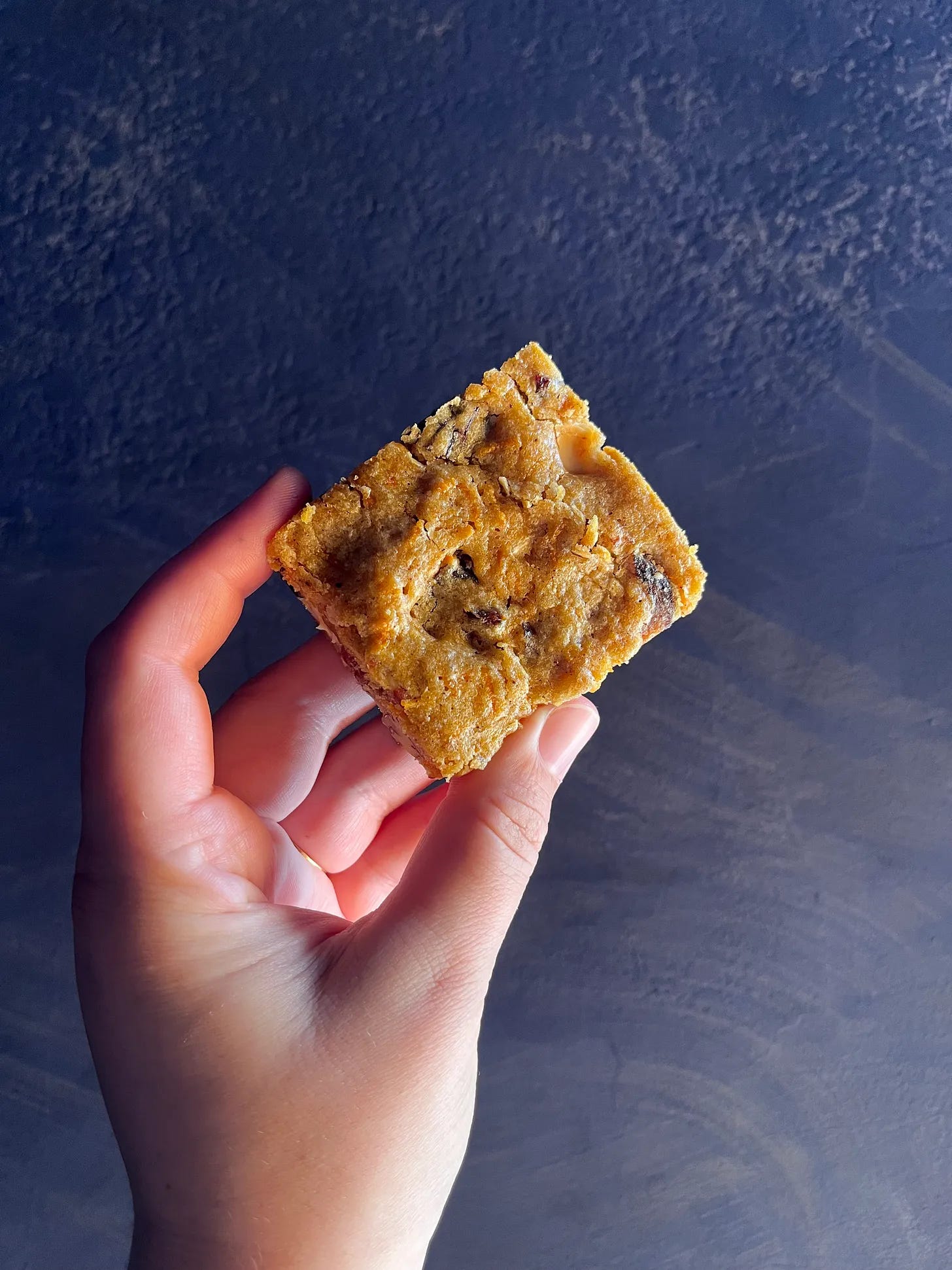 Someone holding up a spiced carrot cake blondie.