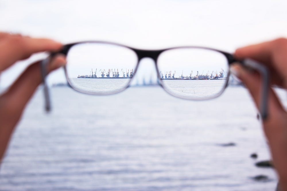 Photo of glasses being held by two hands. We look through the glasses to see a clear picture of the horizon.