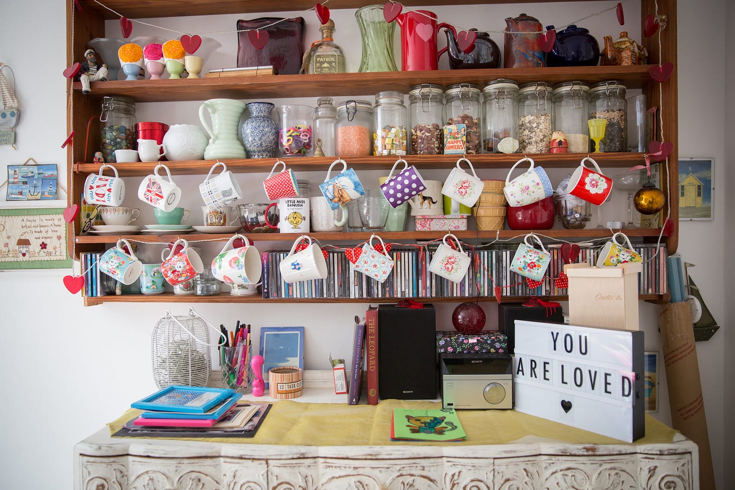 Colorful kitchen cupboard with vasesand hanging mugs and sign saying You Are Loved