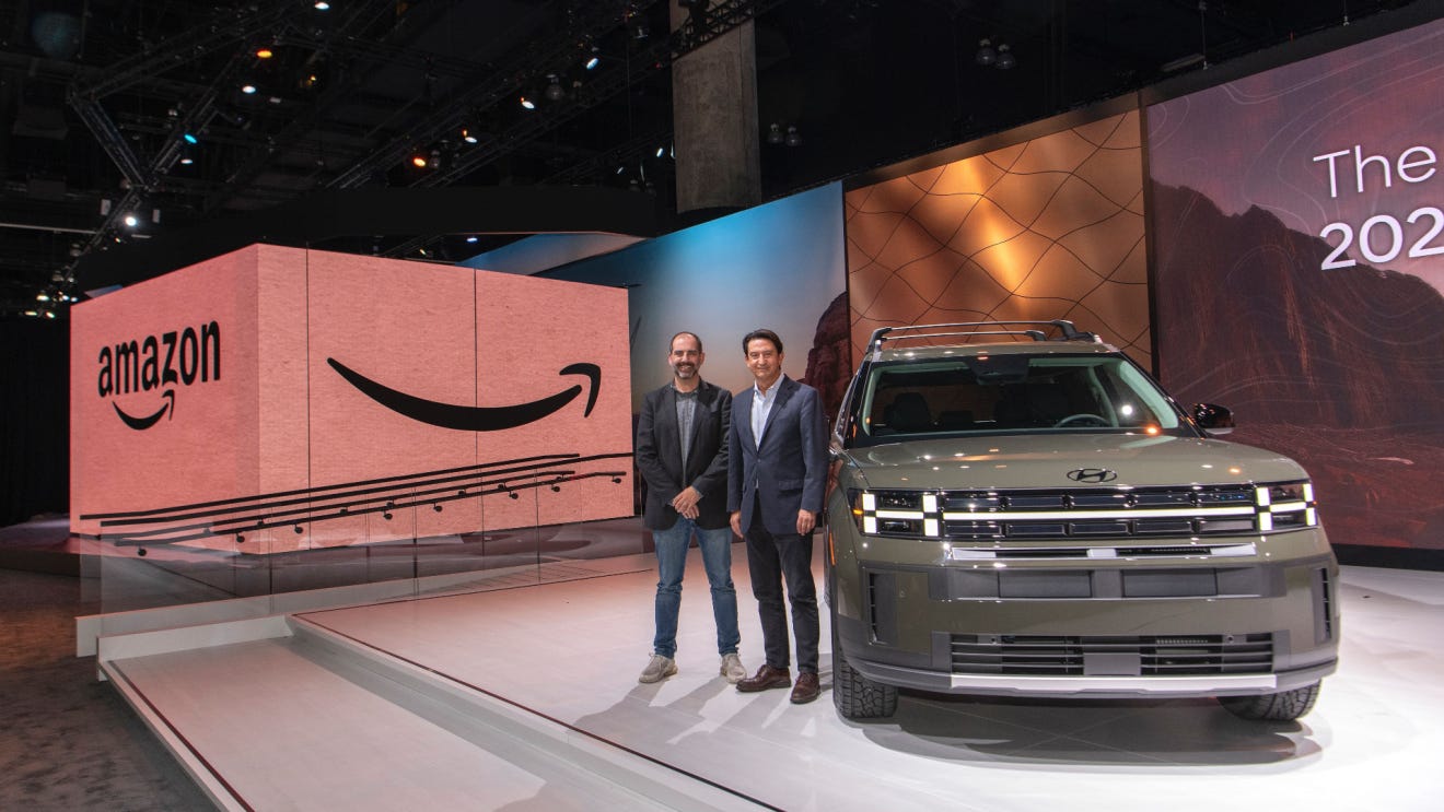 Two people stand on stage next to a Hyundai vehicle. There is an oversized Amazon box behind them.