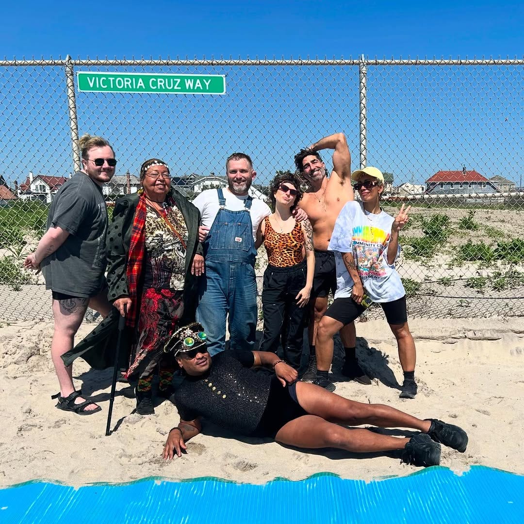 A group of queers poses for a photo on a beach.