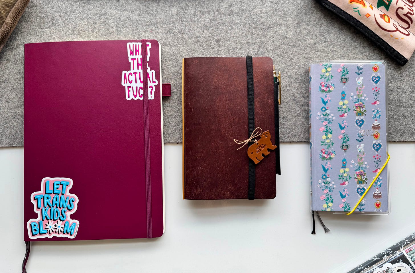 Three notebooks shown on a white desk, with a grey felt desk mat. From Left to Right: B5 Leuchtturm 1917 Monthly Planner (Color: Port Red), Plotter Ring Binder (Bible size, color: dark brown), Hobonichi weeks (Yumi Kitagashi pattern). 