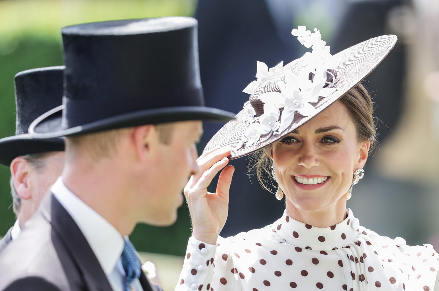 kate middleton smiling and holding her hat at royal ascot