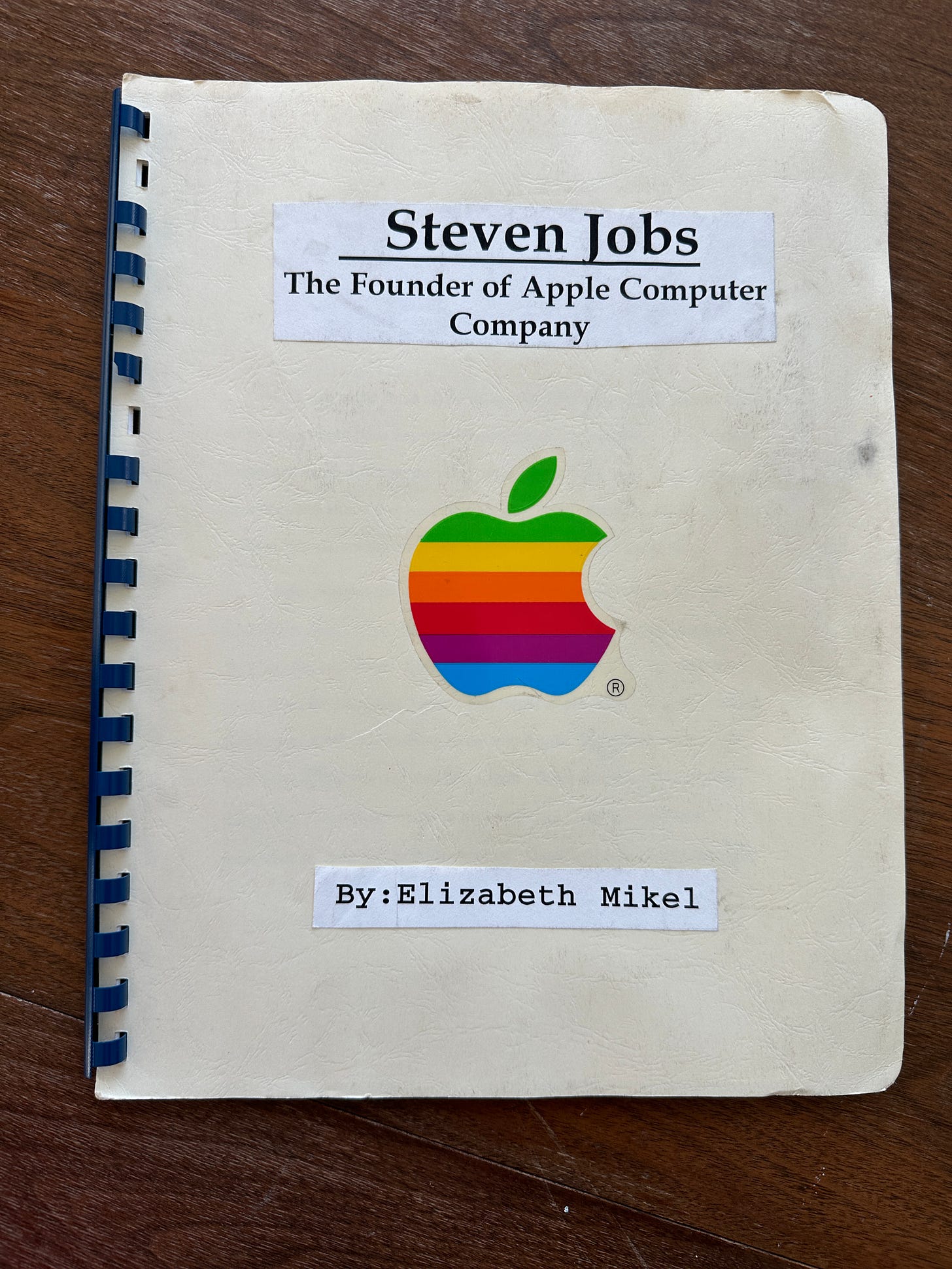 Tan bound report with plastic binding. Has Apple sticker on the front. Title reads "Steven Jobs The Found of Apple Computer Company" by Elizabeth Mikel.
