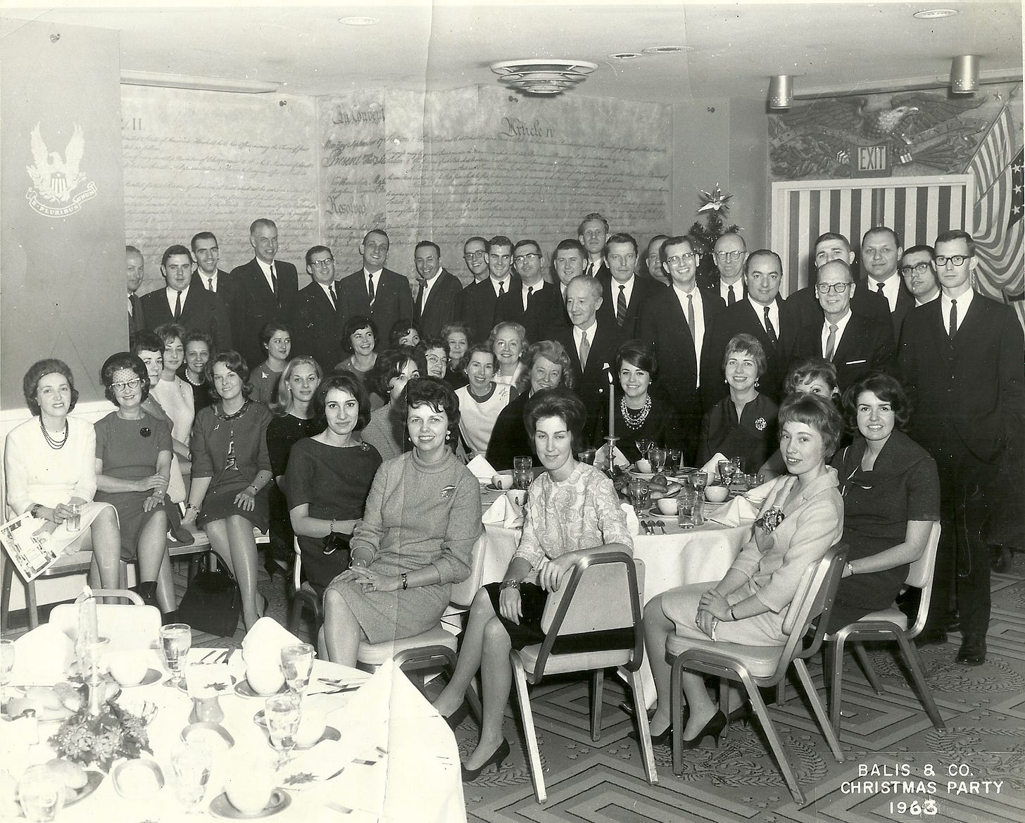 Large group of men in suits and women in dresses gathered at the company holiday party circa 1963