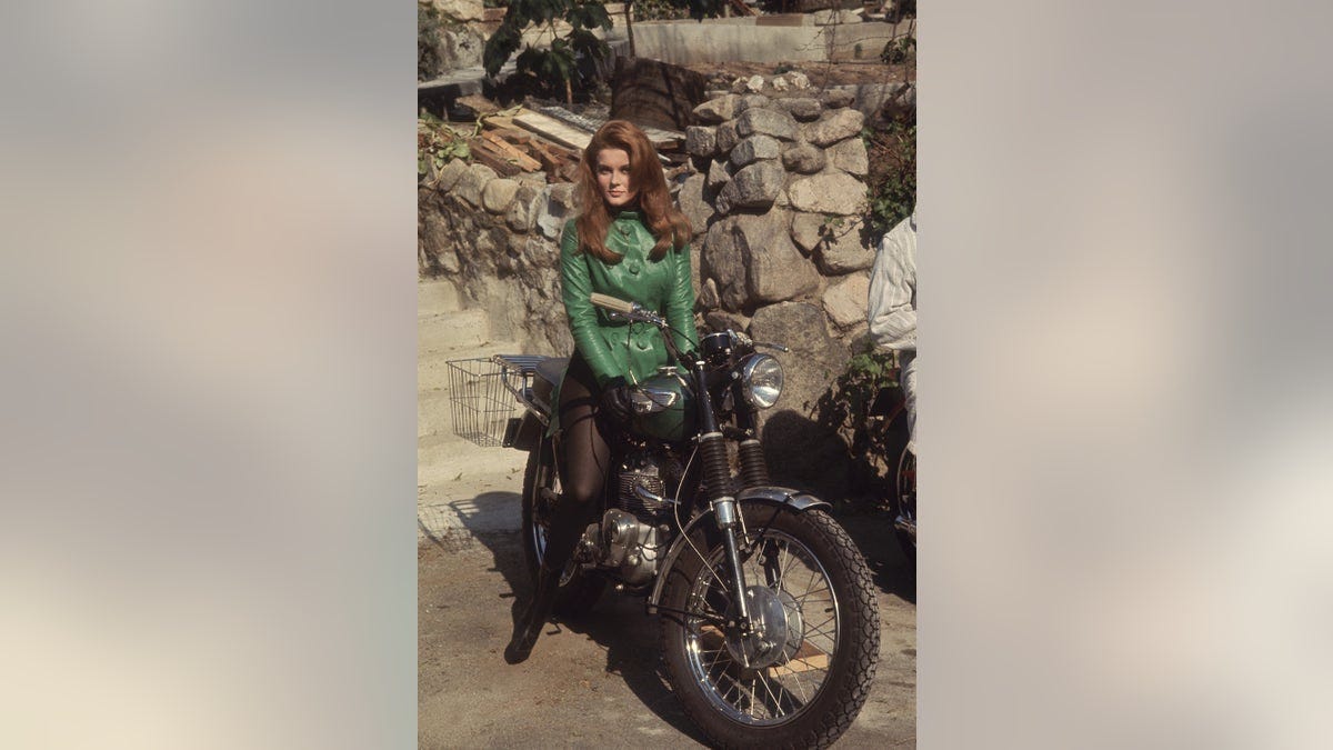 Ann-Margret wearing a green sweater and black stockings on a motorcycle