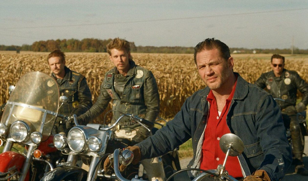 Four men sitting on motorbikes looking at the camera against the backdrop of a cornfield. Most prominently, Benny (Austin Buter) and Johnny (Tom Hardy)