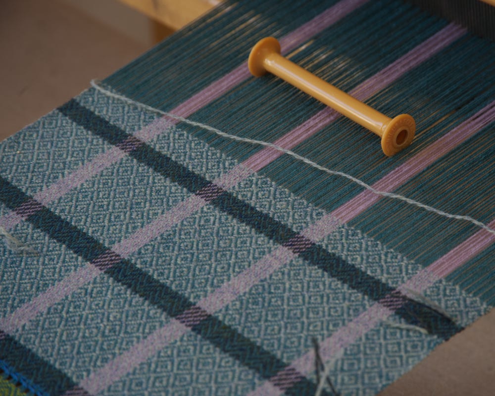 Close up photo of textile being woven on the loom, with an empty bobbin in the upper right corner