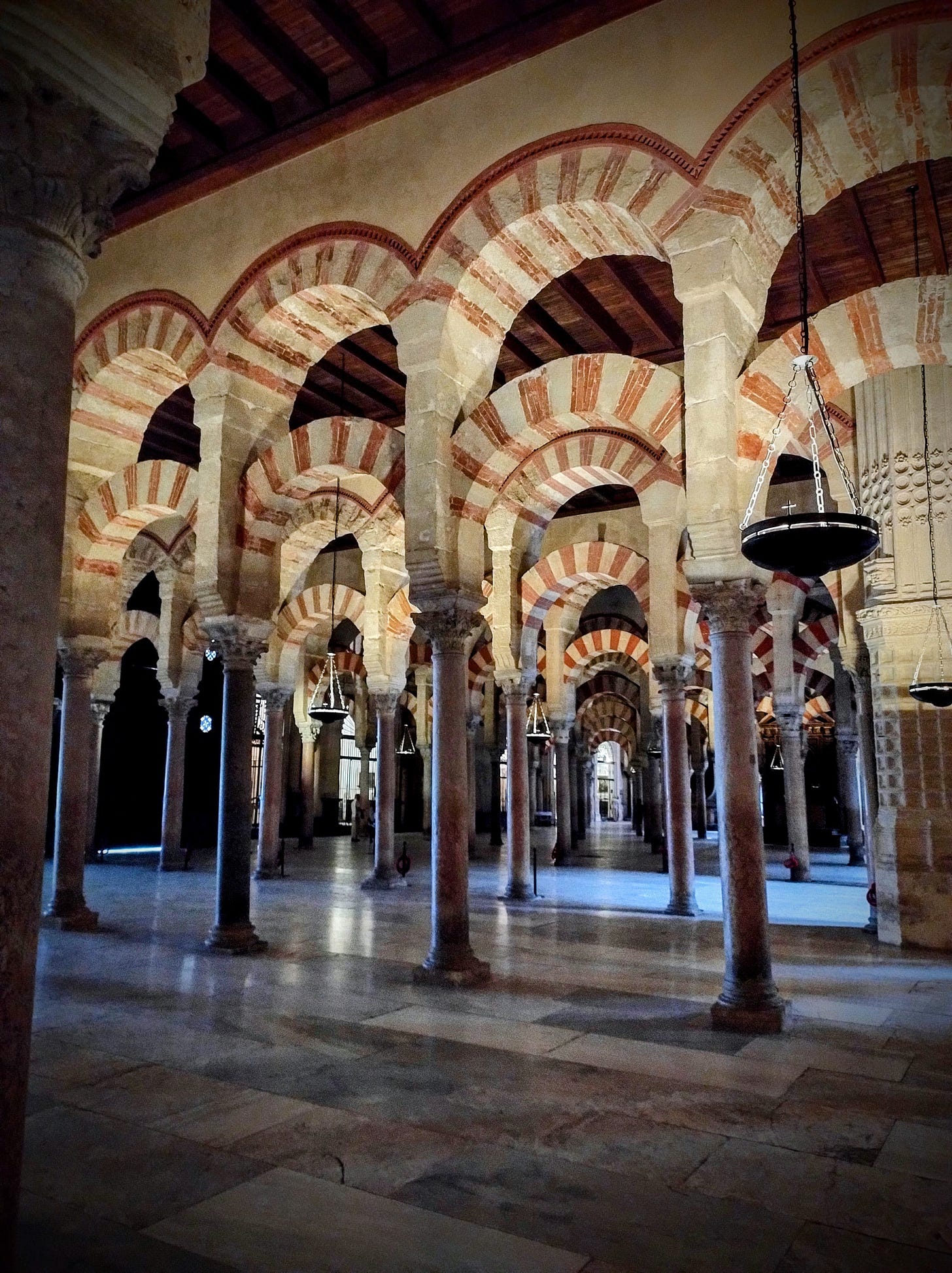 An image showing the Mezquita of Cordoba. There are many repeating arches, with red and white detail as well as a smooth marble floor. 