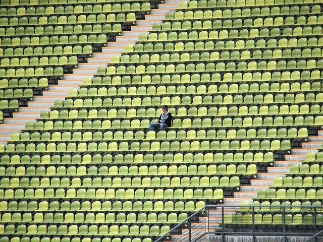 Descrição da imagem: homem sentado sozinho em uma arquibancada de estádio com todos os outros assentos vazios. Se trocar a cor dos assentos de verde para azul, vira o Twitter. Imagem do Pixabay.