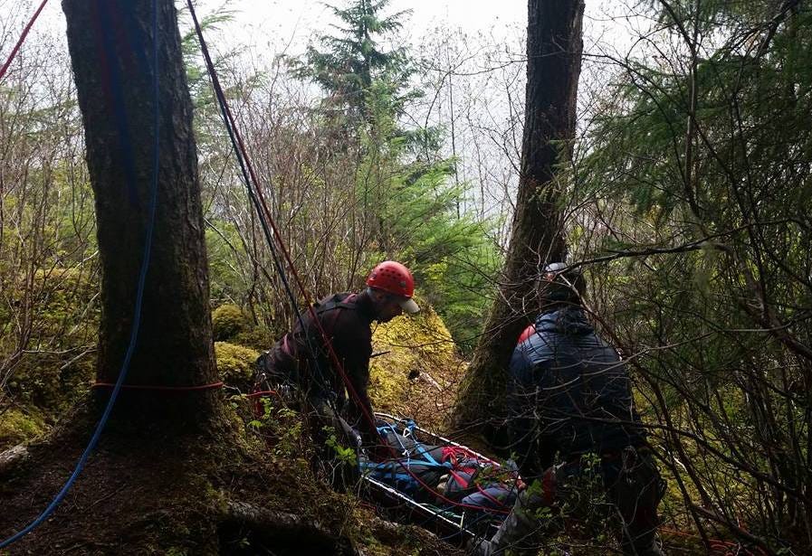 two rescuers packaging someone into a litter at the top of a cliff during a training session