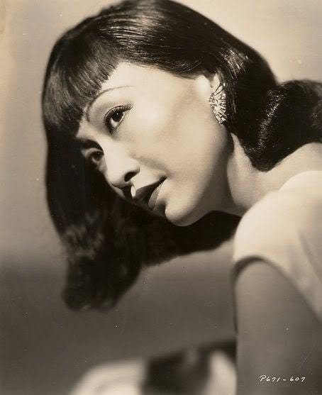 glamour shot of Anna May Wong from the side, her hair shoulder length, she's wearing a white dress and an art deco style earring