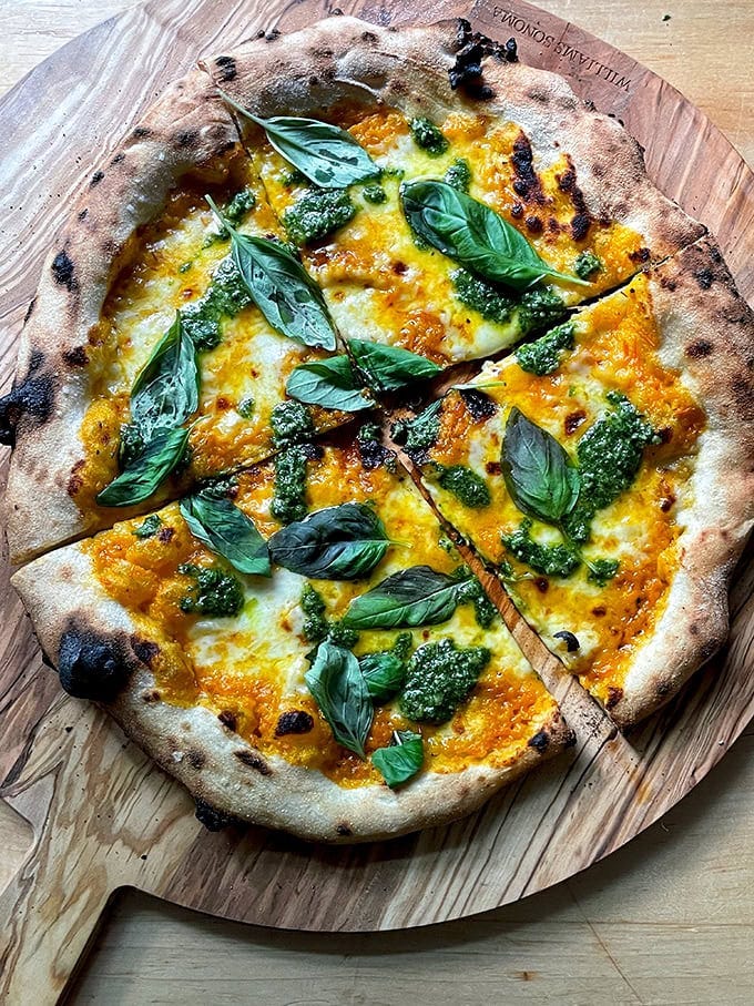 A pizza topped with yellow tomato sauce, basil pesto, and basil. 