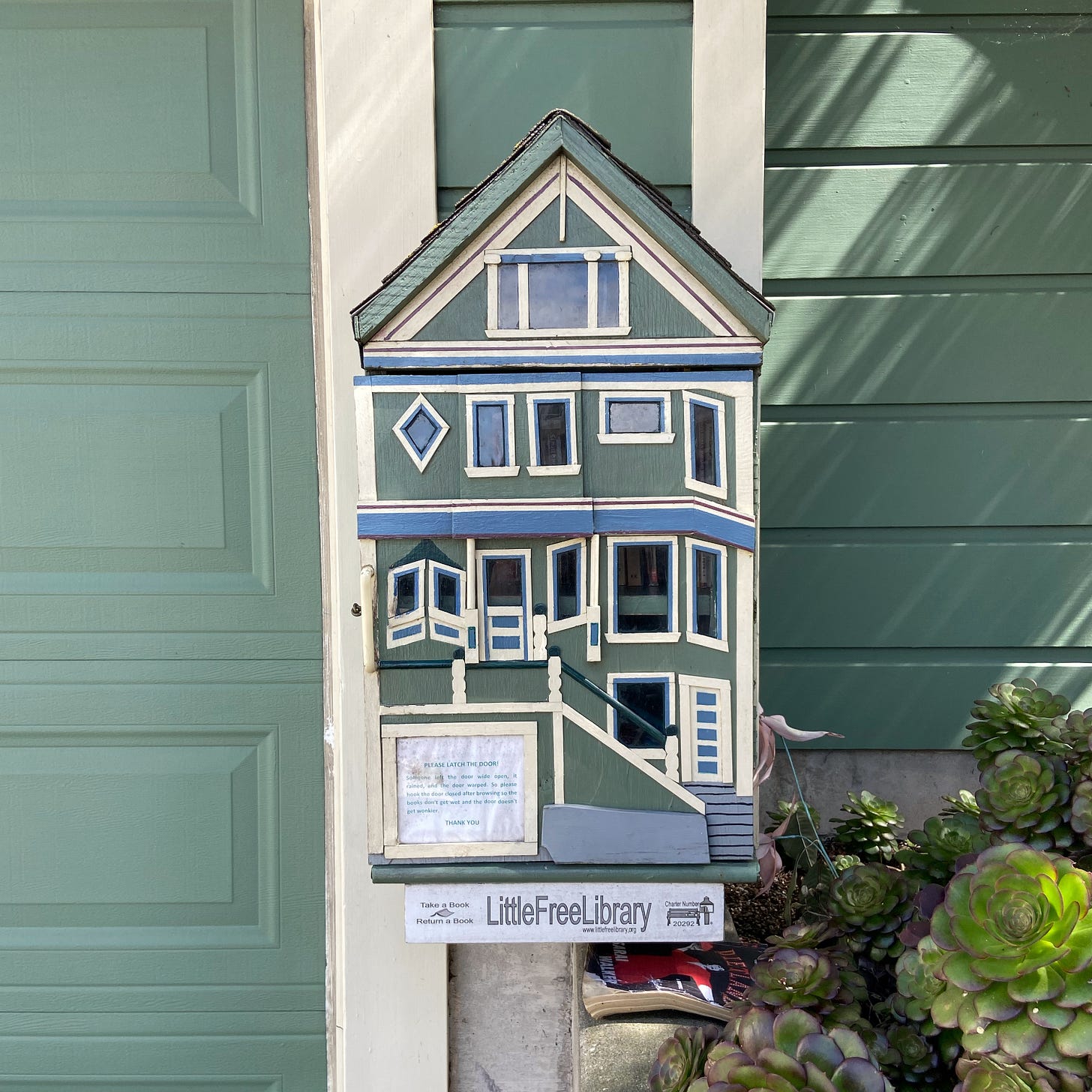 A dollhouse style little free library in front of a house in California
