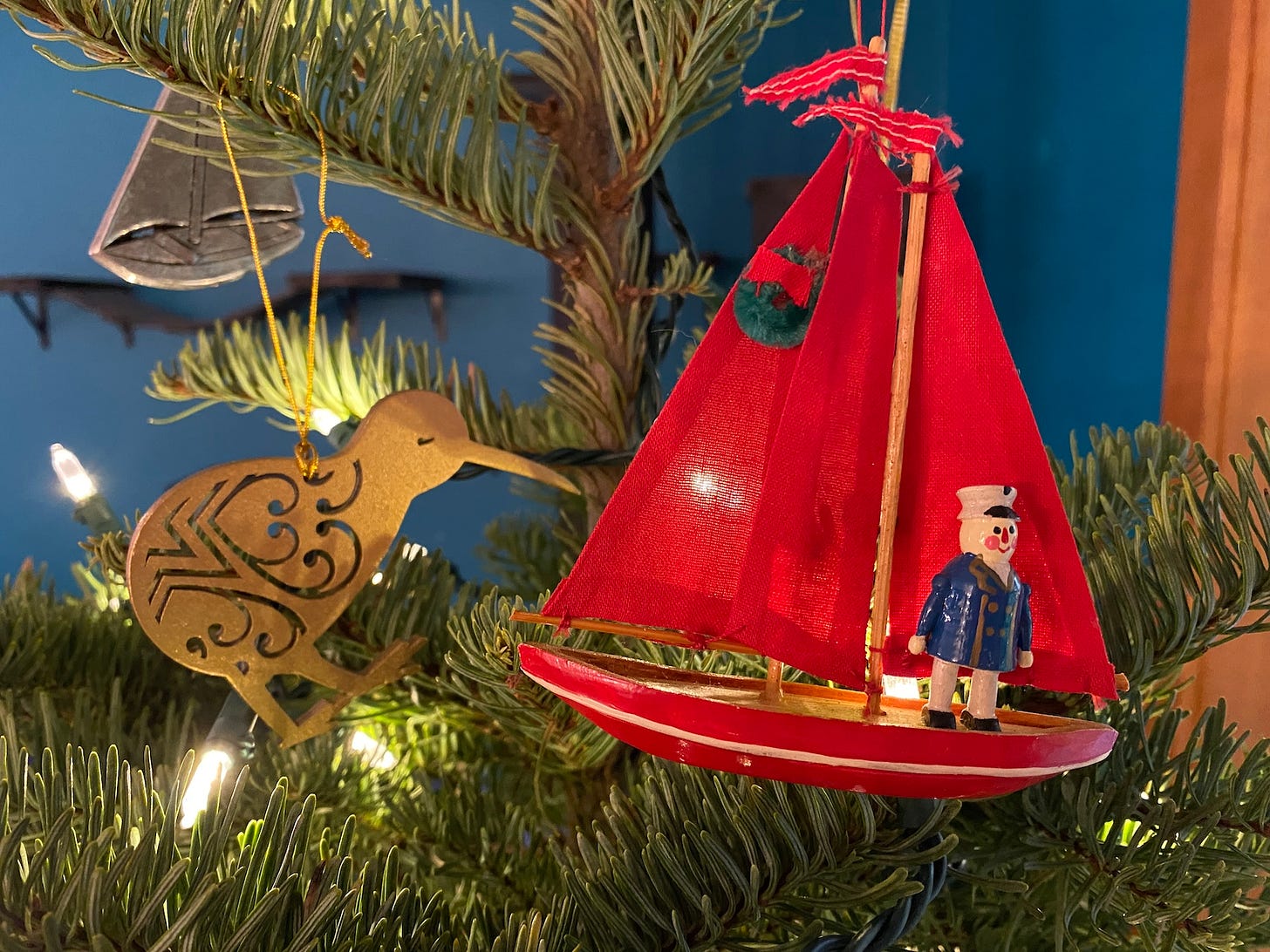 Very close up photo of a Christmas tree with a red fabric sailboat ornament and a carved kiwi bird ornament