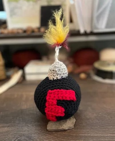 A crochet f-bomb. Humor as a way to manage anxiety. In portrait mode with general desk litter in the background)