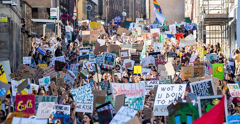 People in crowded streets at a protest, holding many different climate-change related signs