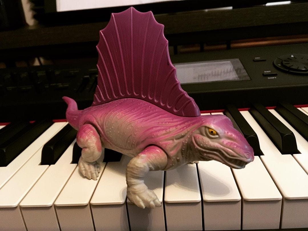 A pink dimetrodon in a semi-sprawled stance looking mean atop a piano keyboard.