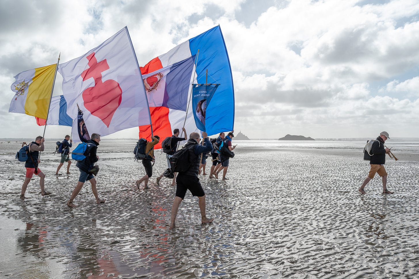 Knights process with Catholic flags, as Mont-Saint-Michel is seen in the distance. Knights process with Catholic flags, as Mont-Saint-Michel is seen in the distance.