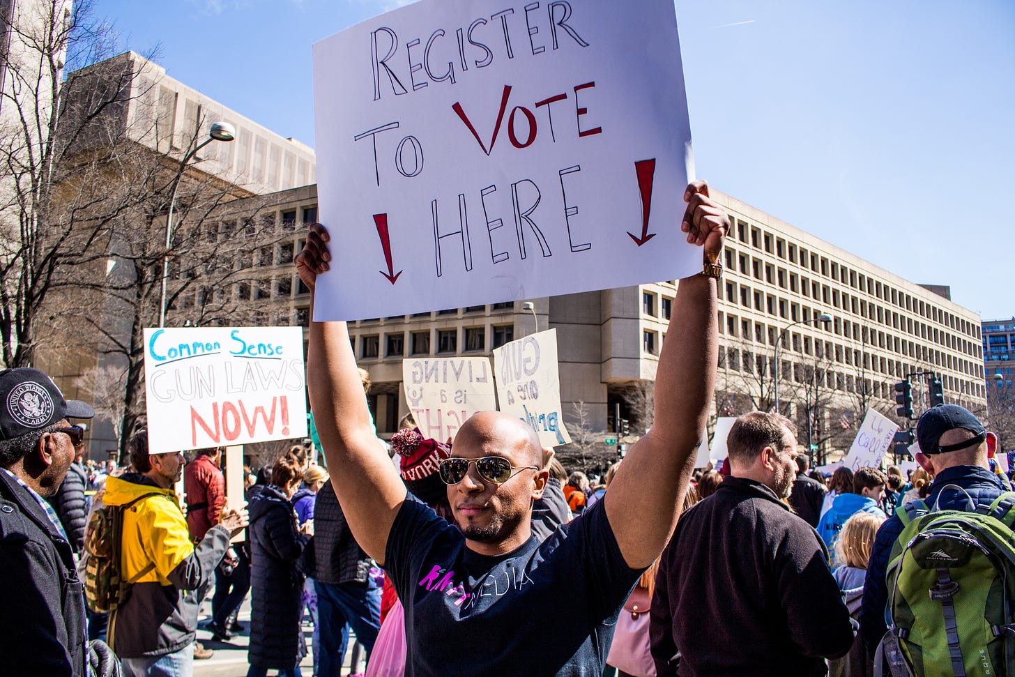 A photo of Ahmed Baba holding up a "Register To Vote Here" sign at the March of Our Lives in 2018