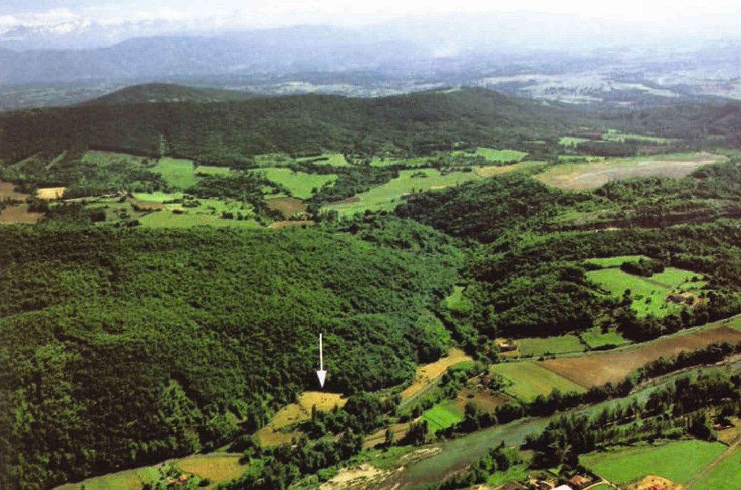 A landscape with forest-covered hills, a valley floor, and an arrow pointing to a place immediately against a rock face A landscape with forest-covered hills, a valley floor, and an arrow pointing to a place immediately against a rock face