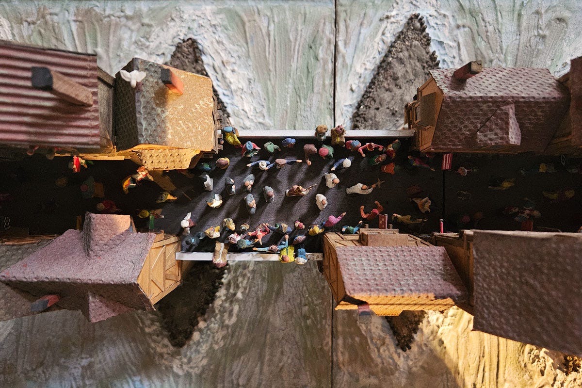 looking down on a model of houses on a bridge with many people walking along the road