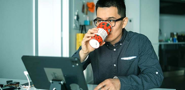 Photo of a man drinking from a coffee cup while watching a screen.